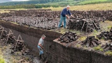 Twee mannen steken turf in een open veenveld met stapels turf